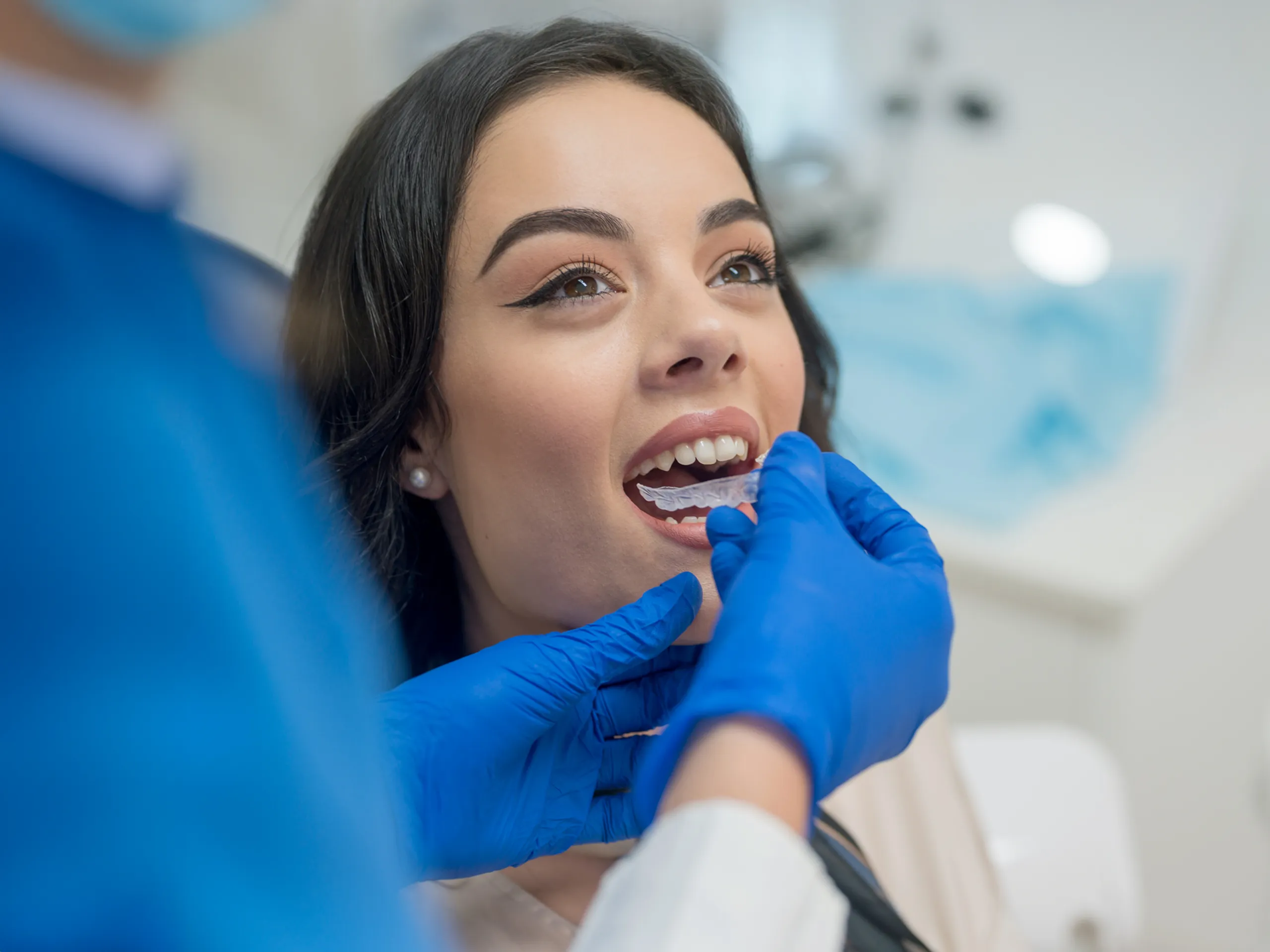 Female dentist inserts a transparent dental aligner for a patient.
