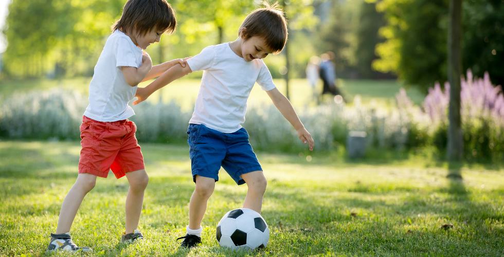Twee kinderen voetballen op een veldje